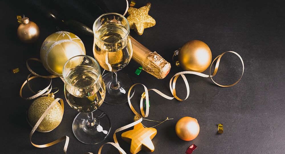 Two glasses of champagne bottle golden christmas toys serpentine star balls on a black background. New Year concept.