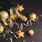 Two glasses of champagne bottle golden christmas toys serpentine star balls on a black background. New Year Christmas concept. Festive minimalism. Horizontal frame. Flat style layout